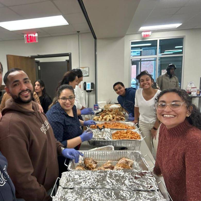Smiling volunteers serving trays of food at a St. Verena's Outreach Program meal